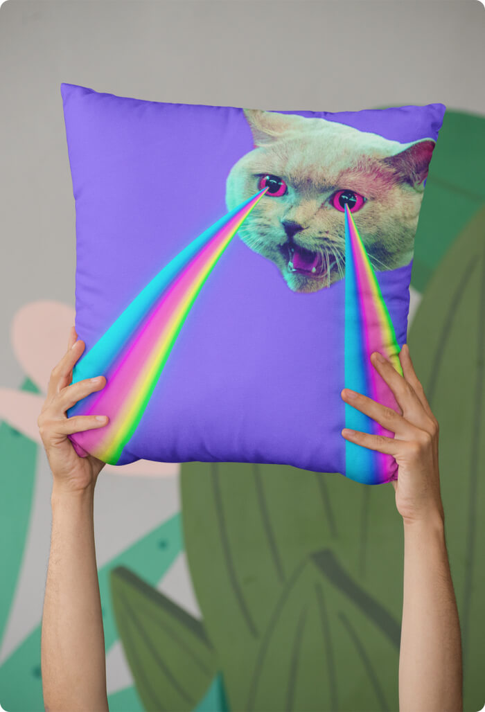 A mockup image of a custom pillow with a cat shooting rainbows from his eyes print.