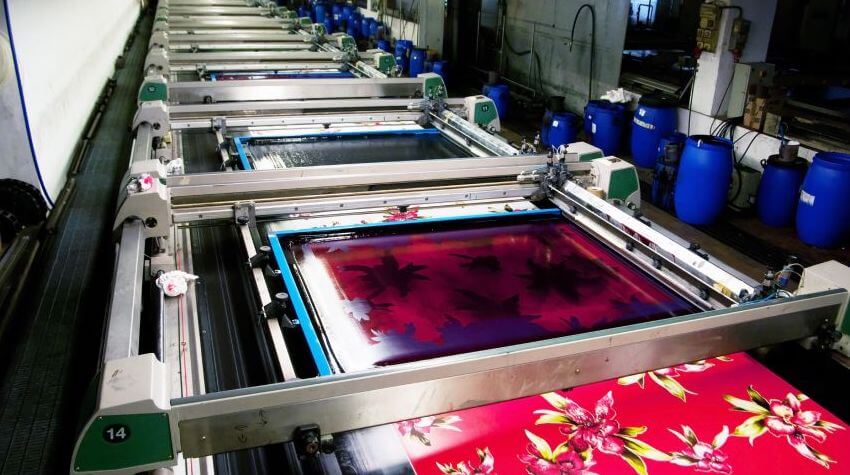 Dye sublimation machinery printing a colorful red floral pattern on large pieces of fabric.