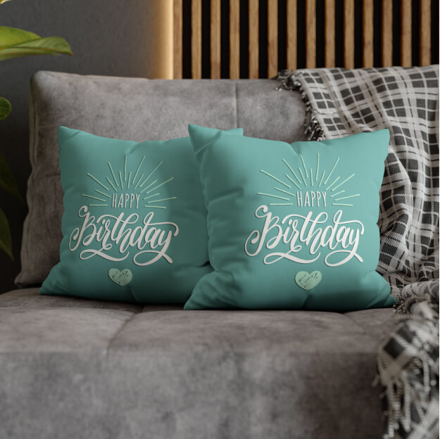 Close-up of a grey sofa with two green pillows that say “Happy Birthday”
