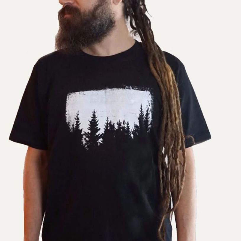 A man with dreadlocks wearing a black t-shirt with an abstract forest created in the negative space with white dye.