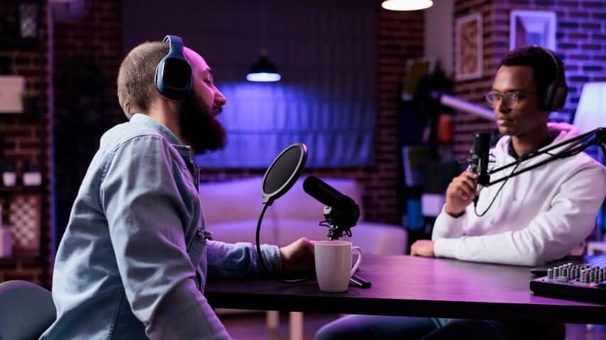 Two men in a studio with ambient purple lights, recording a podcast.