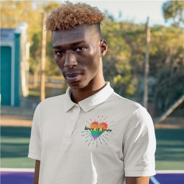 Lifestyle portrait of a model posing in a custom polo shirt with a rainbow heart design and the slogan “Love is Love” printed on the upper left chest.