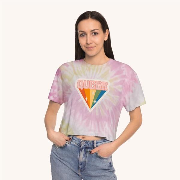Model posing with a custom tie-dye spiral shirt with the design of a rainbow and the word “Queer” in the shape of a diamond printed on the chest.