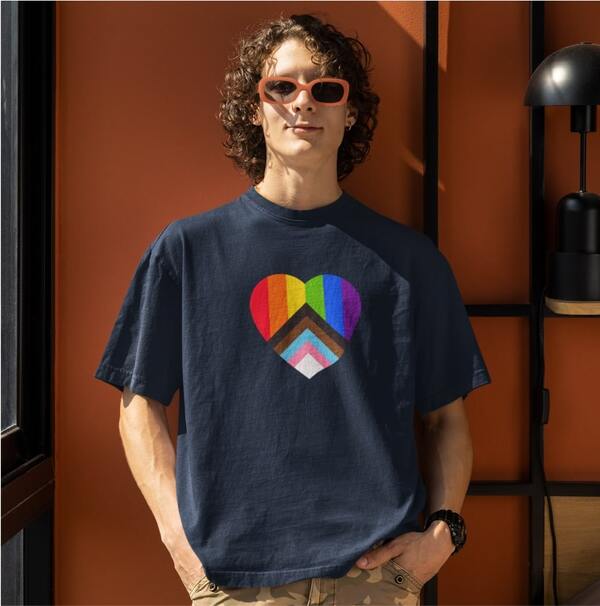Lifestyle photo of a model posing in a custom t-shirt with an image of the Progress Pride flag in the shape of a heart printed on the chest.