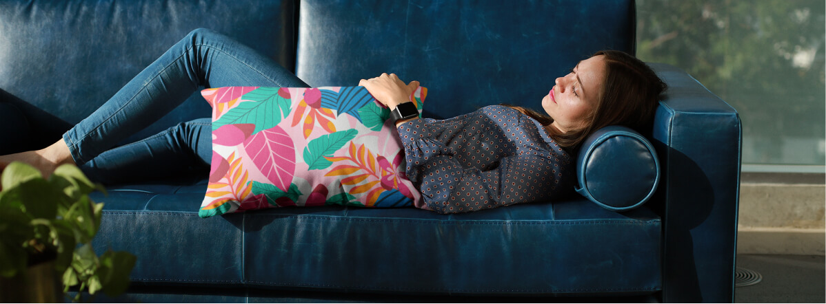 An image of a woman lying on a couch, holding a personalized pillow with abstract graphics.