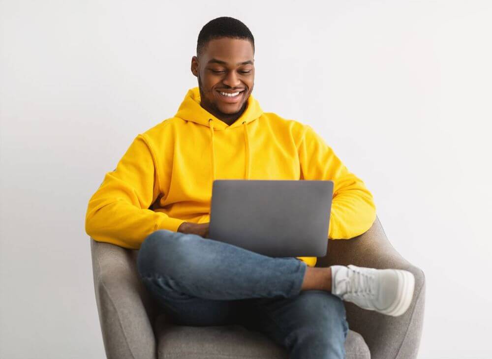 A guy sitting in a comfortable chair with a laptop, having a good time running his business risk-free.