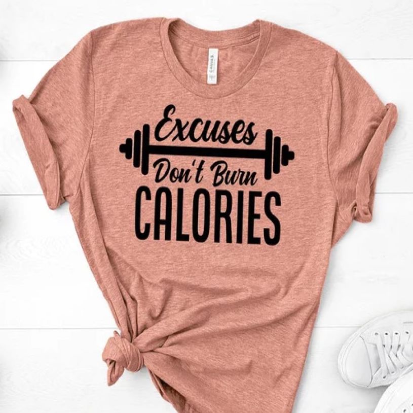 Salmon-colored t-shirt that says, “Excuses Don't Burn Calories” with a black cartoon barbell in the middle of the writing.