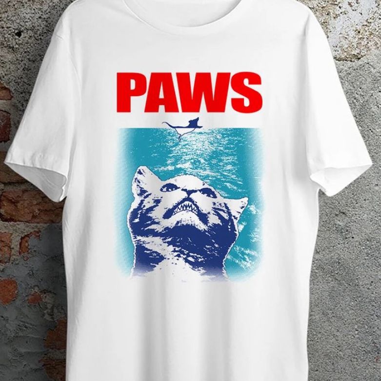 A white t-shirt with a parody of the movie Jaws with an angry kitten underwater staring straight at a mouse and the word PAWS written in red on top.