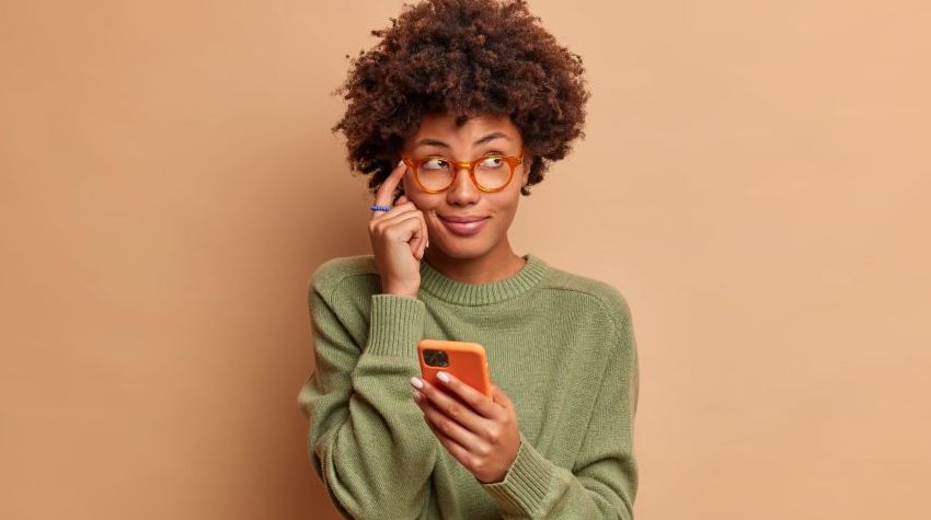 Woman with glasses holding a phone with a thoughtful expression.