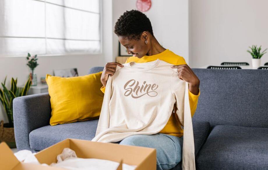 A young woman checking a sample of a custom beige long sleeve tee that says “Shine”