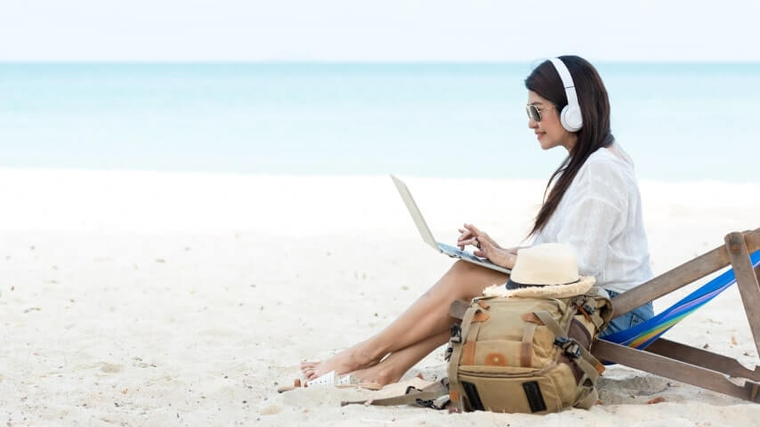 Woman working as a freelancer on her laptop from the beach.