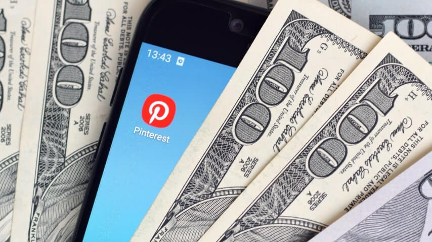 Phone placed between dollar bills, showing the Pinterest app icon.