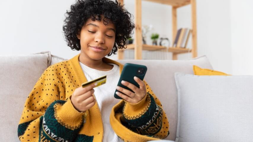 Young, smiling woman holding a phone and a credit card.