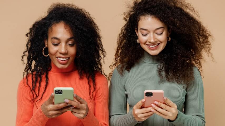 Two women smiling at their phones while working on affiliate marketing on Pinterest.