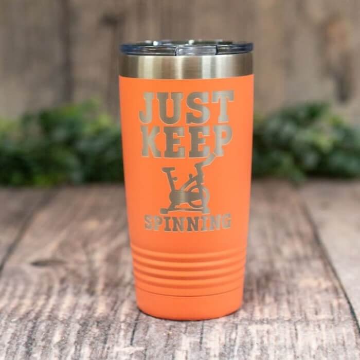 Orange tumbler with a design of a stationary bike and the caption “Just keep spinning.”