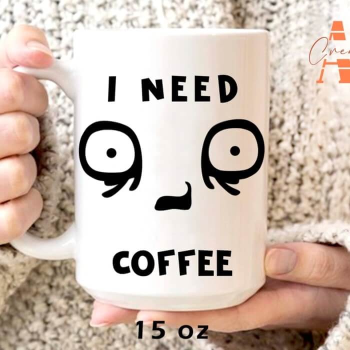 Large white ceramic mug with a design of a tired cartoon face and the caption “I need coffee.”