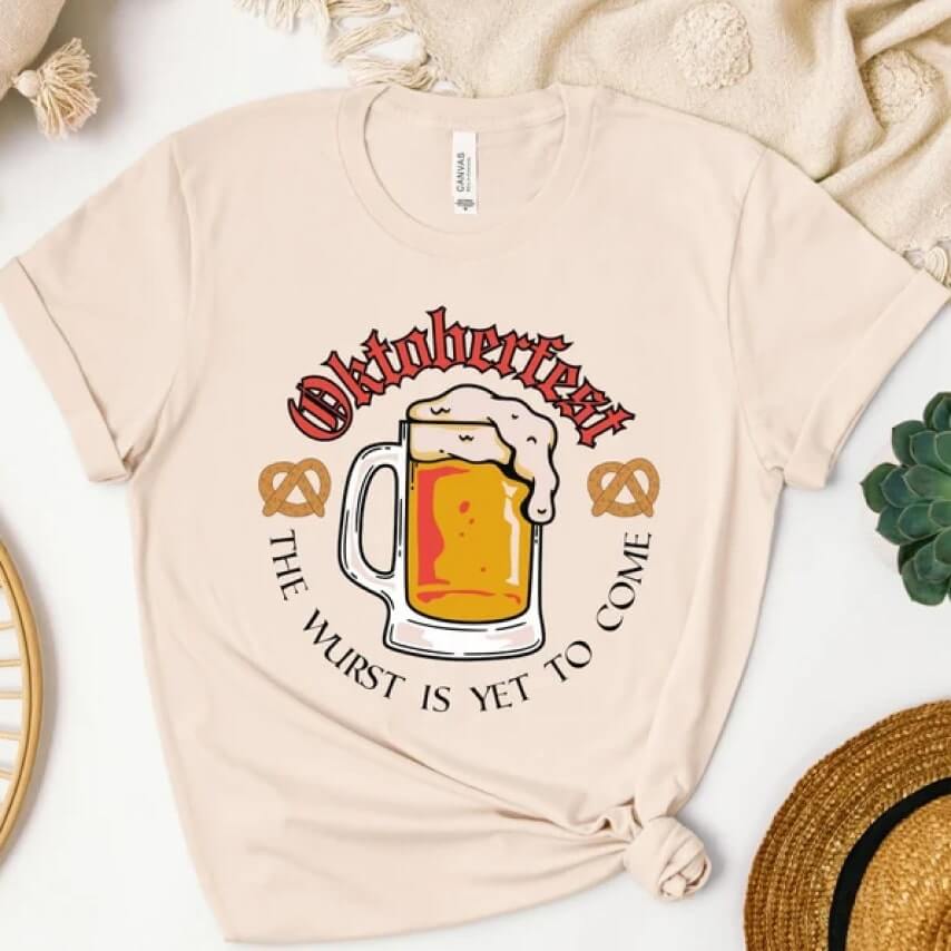 Beige t-shirt with a graphic of a beer mug and the text, “Oktoberfest: the wurst is yet to come.”