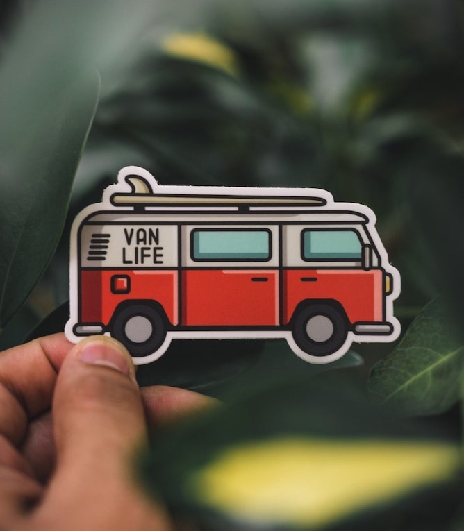 Person holding a custom sticker of a red and white van with the text “Van Life” on it.