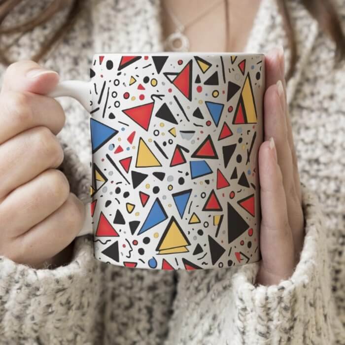 Woman holding a white mug with a pattern of colorful geometric shapes.