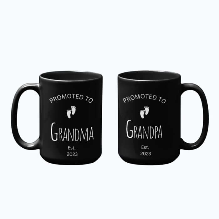 Two black mugs with graphics of tiny baby feet and the captions “Promoted to grandma” and “Promoted to grandpa est. 2023.”