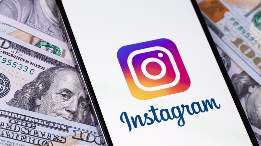 Phone with the Instagram logo on the screen placed on a pile of dollar bills.