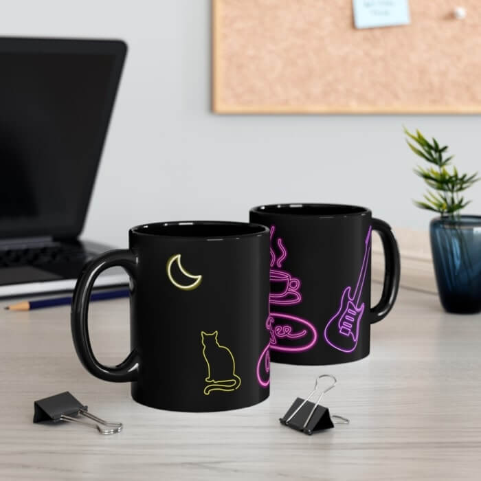 Two black mugs with neon colored designs of a cat, guitar, moon, and other elements.