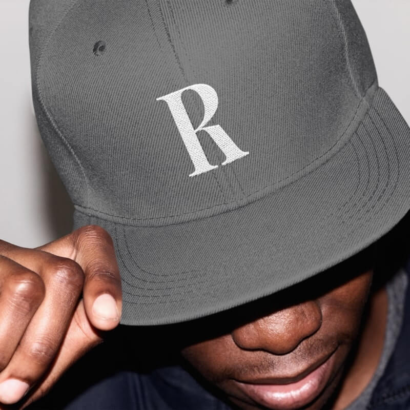 An image of a man wearing a custom hat in gray with the letter “R”.