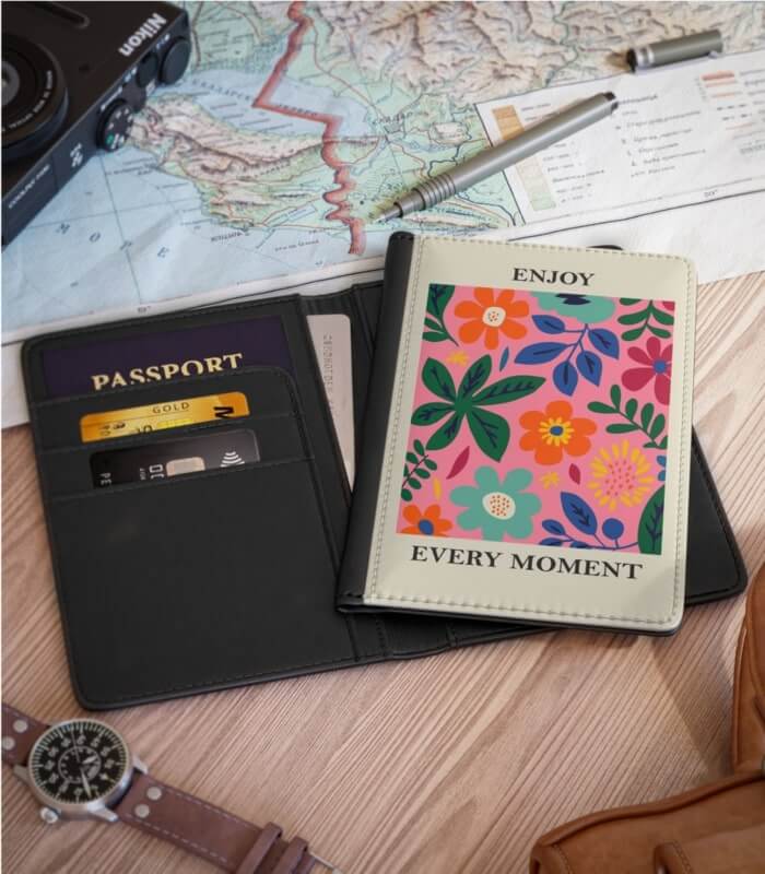 A table decorated with a world map, a sophisticated wristwatch, and an eye-catching passport holder with a vibrant floral print and an inspiring mantra 'Enjoy Every Moment.'