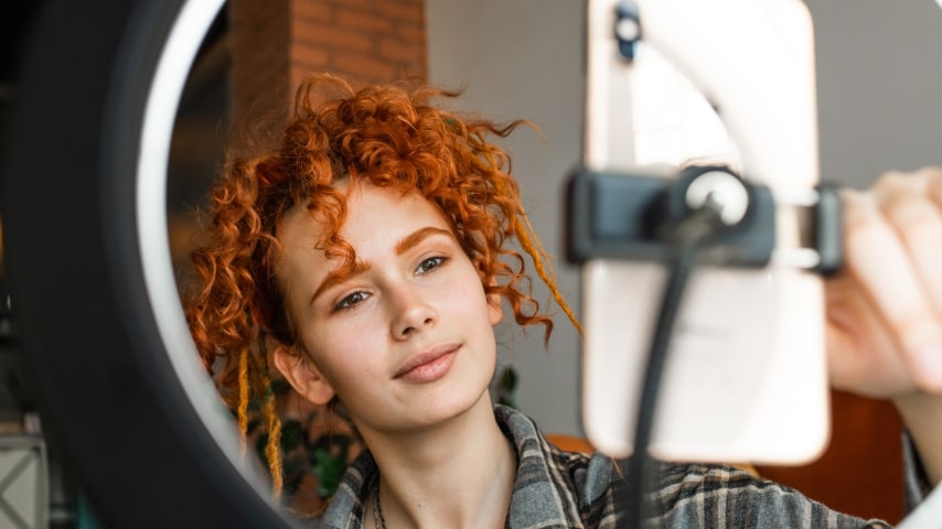 Young woman filming an Instagram Reels video using her phone and a ring light.