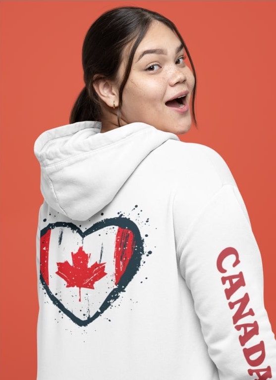 An image of a woman wearing a custom hoodie with Canada written on her sleeve and a heart-shaped Canadian flag on the back.