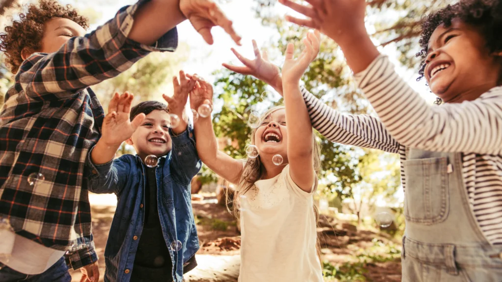 Children joyfully playing in the park, raising their hands in excitement under a clear blue sky.