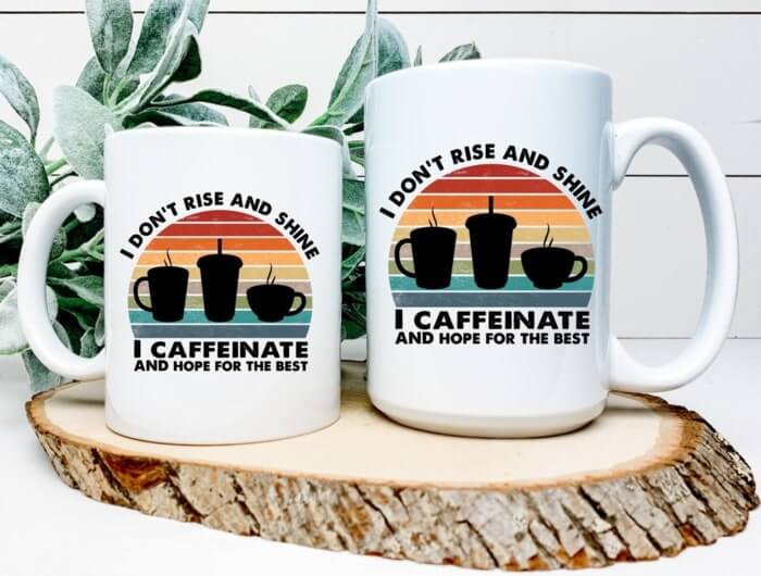 Two white mugs with a graphic of three different cup silhouettes and the caption “I don't rise and shine, I caffeinate and hope for the best.”