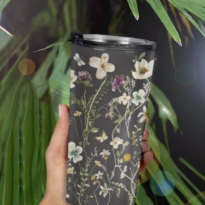 Vacuum insulated tumbler with a pattern of flowers on a mossy green background.