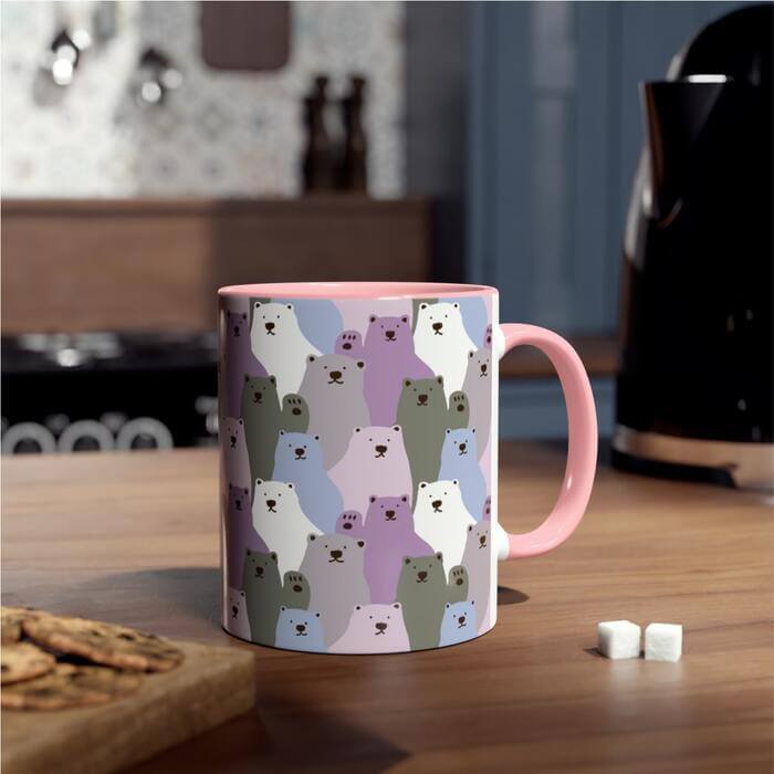 A charming pink mug elegantly positioned on a table, adorned with an all-over print featuring cute, animated bears in blue, purple, green, white and grey