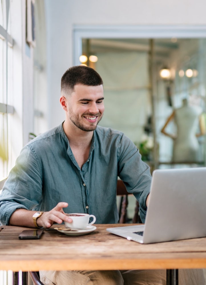 Man drinking a coffee and smiling while working on his laptop.