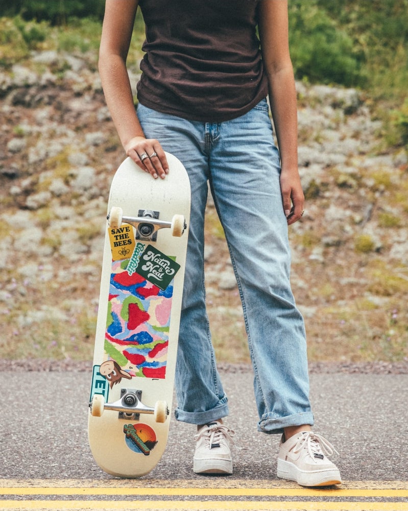 Person holding a skateboard covered in various colorful custom stickers.