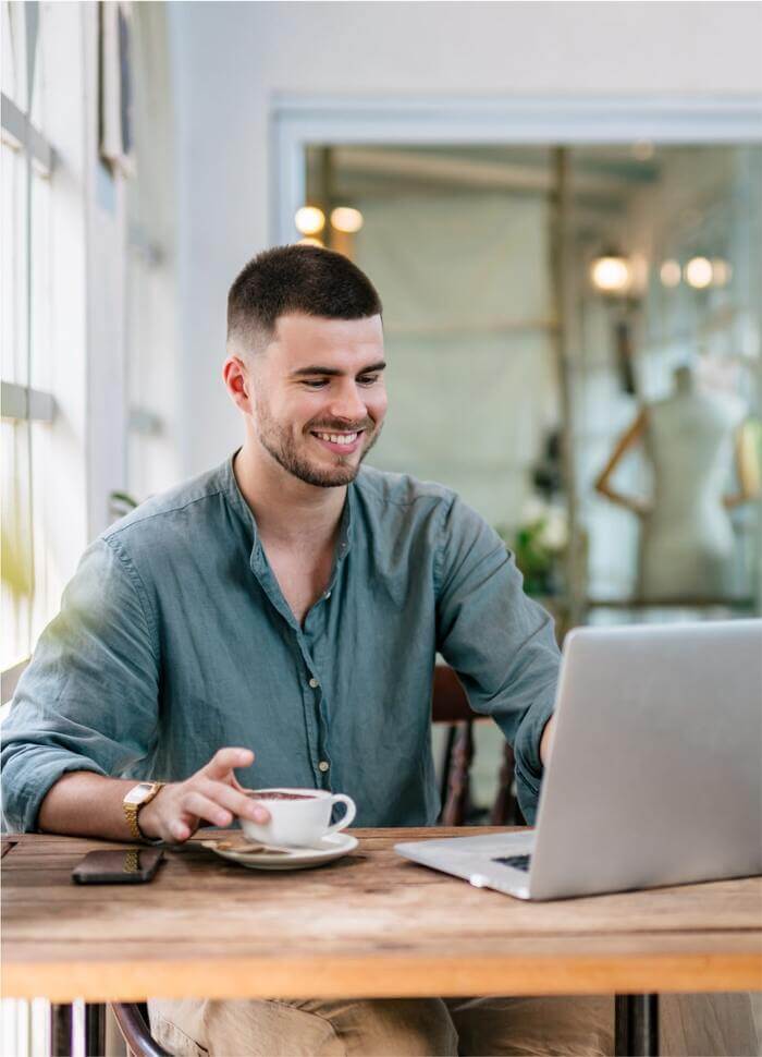 A young man enjoying a cup of coffee while setting up his Printify account on the laptop.