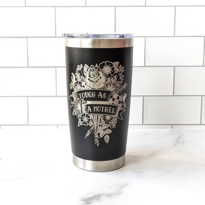 Black coffee tumbler with a design of silver flowers and the caption “Tough as a mother.”