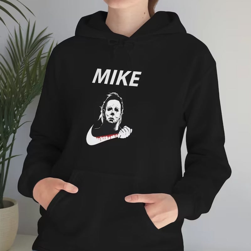 Woman wearing a black hoodie with an image of a masked horror movie character holding a curved knife and the caption “Mike” above it.