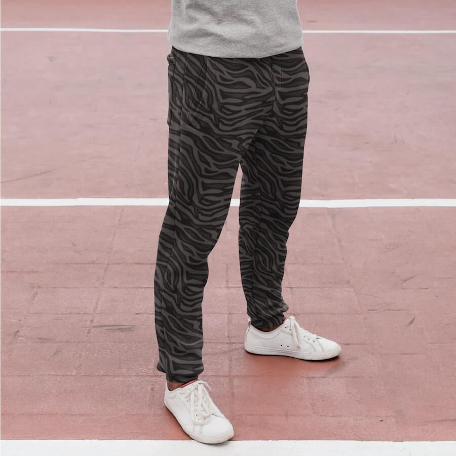 A person wearing white sneakers and dark gray joggers with an animal light gray subtle pattern