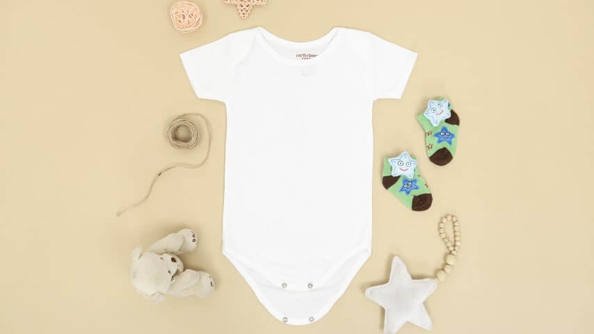 A blank white baby bodysuit surrounded by baby toys.