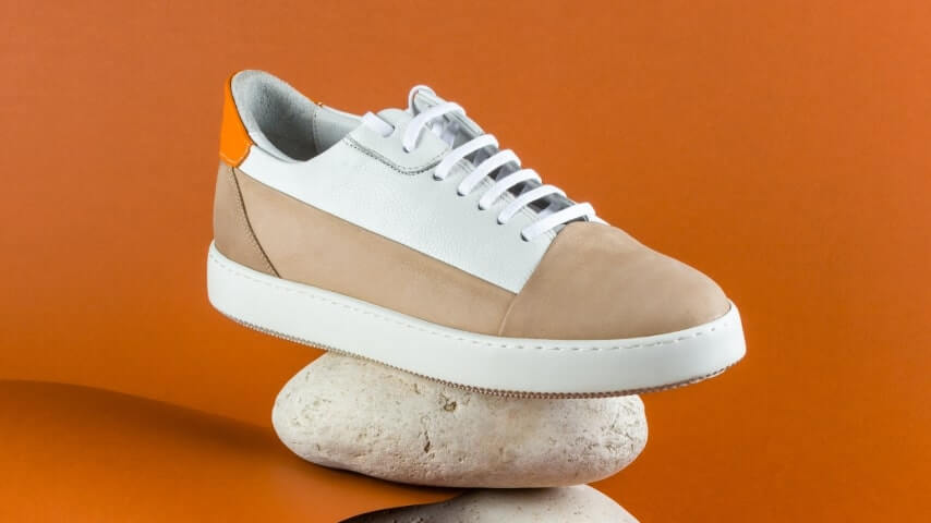 A sneaker in white, light brown, and orange colors placed on a rock.