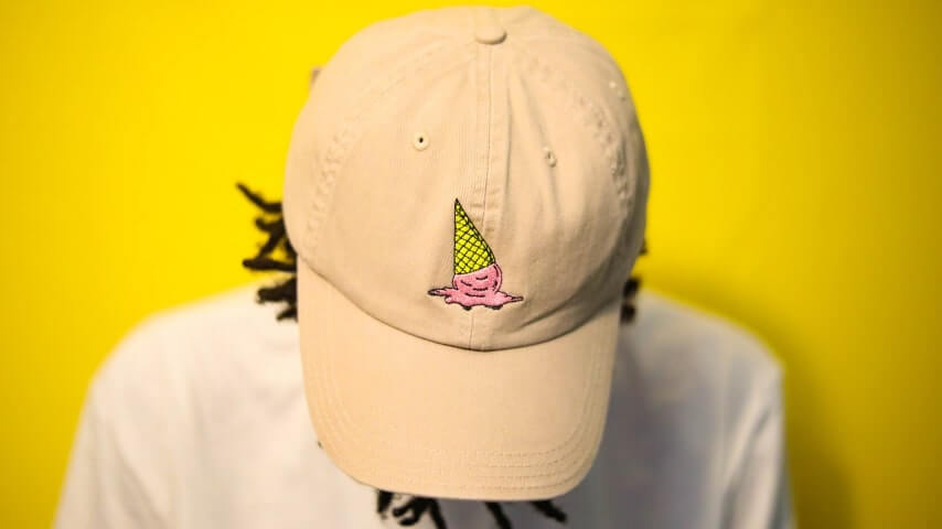Person wearing a beige cap with an embroidered design of a dropped ice cream cone.