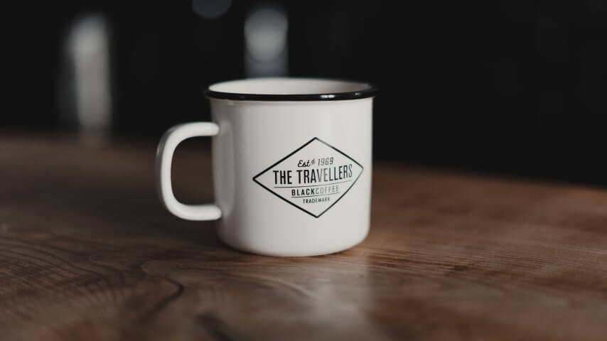 White enamel camping mug with a logo text: “The Travelers' Black Coffee.”