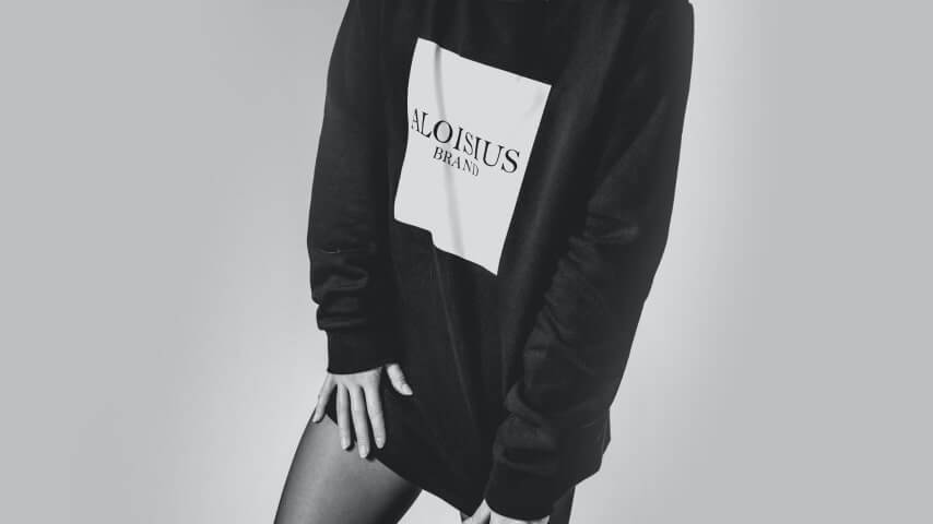 Woman wearing a long, black over-sized sweatshirt with a brand logo printed on the front.