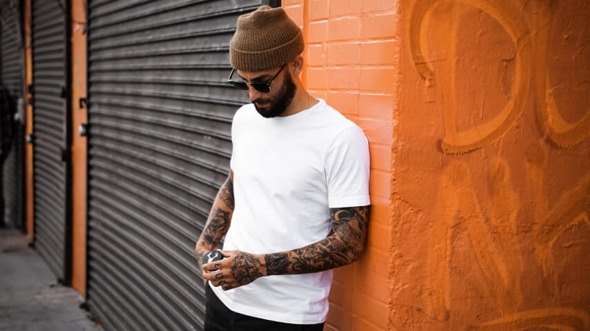 Man in sunglasses and a white t-shirt leaning against a wall.