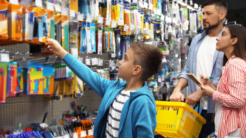 A boy in a store with his parents, shopping for school essentials for the upcoming school year.
