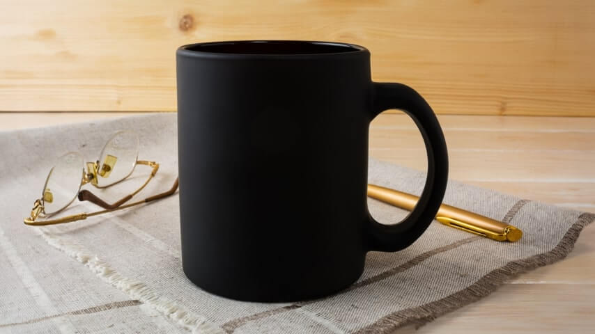 Black mug in a minimalistic vintage setting next to a pair of glasses and a golden pen.