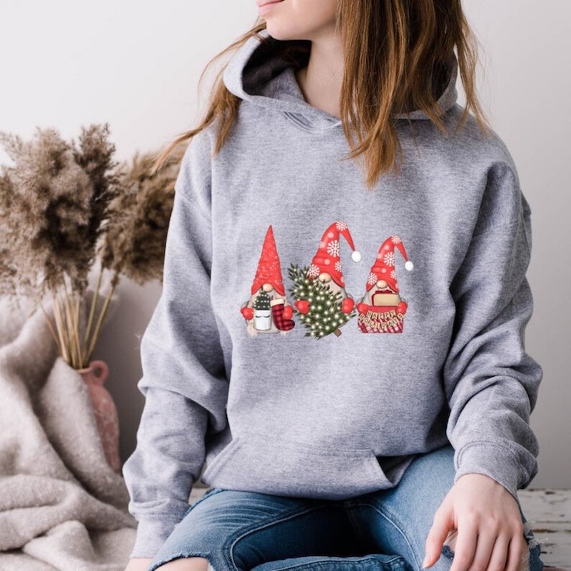 Gray hoodie with a design of three gnomes holding Christmas trees and gifts.