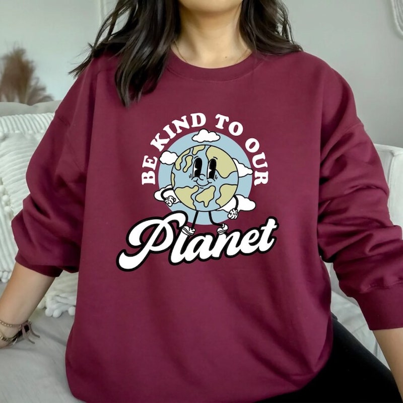 Maroon sweatshirt with a design of an anthropomorphic, smiling planet Earth and the text around it saying, “Be kind to our planet.”